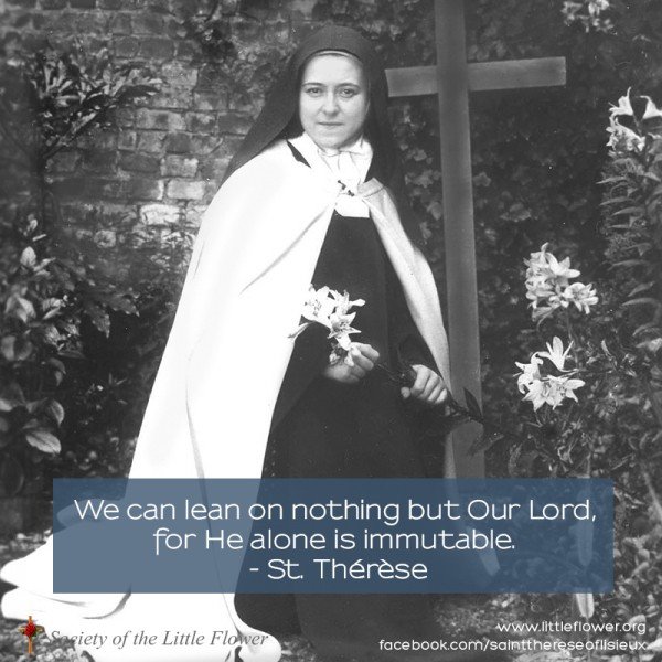 Photo of St. Therese of Lisieux, holding an Easter lily, in the garden at Le Carmel monastery,  before a wooden cross.