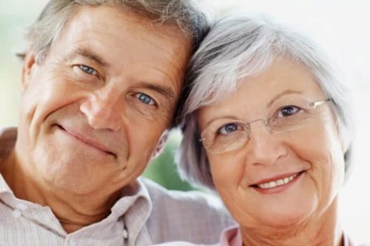 Older couple with heads touching, smiling at camera