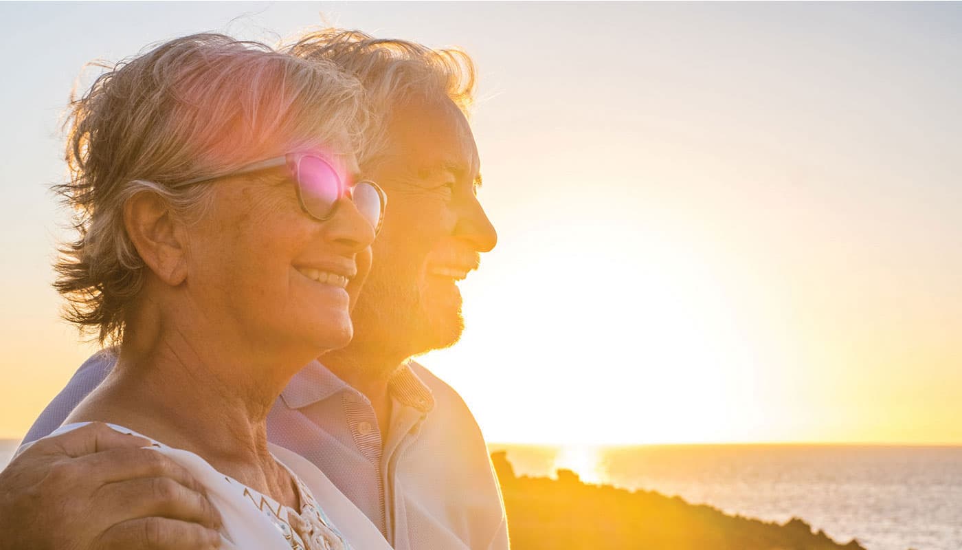 Older man and woman, backlit by sun, looking out over the water