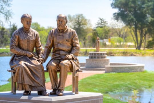 Bronze statue of Sts. Louis and Zelie martin with pond and bronze statue of St. Therese in the back